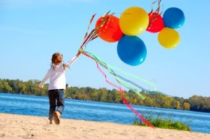 little gile running along the beach with ribbons and balloons
